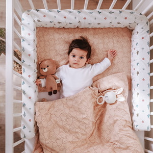 Baby im Gitterbett mit kuscheliger Bettschlange und Bettwäsche