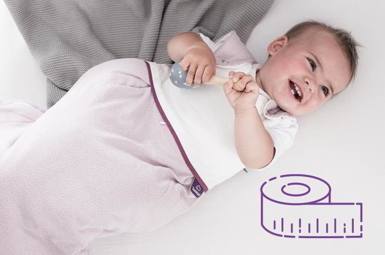 Baby im rosa Träumeland Schlafsack im Bett mit Illustration von einem Maßband