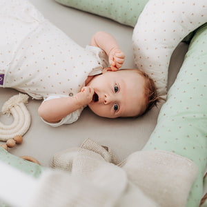 Baby im Bett liegend mit Bettschlange
