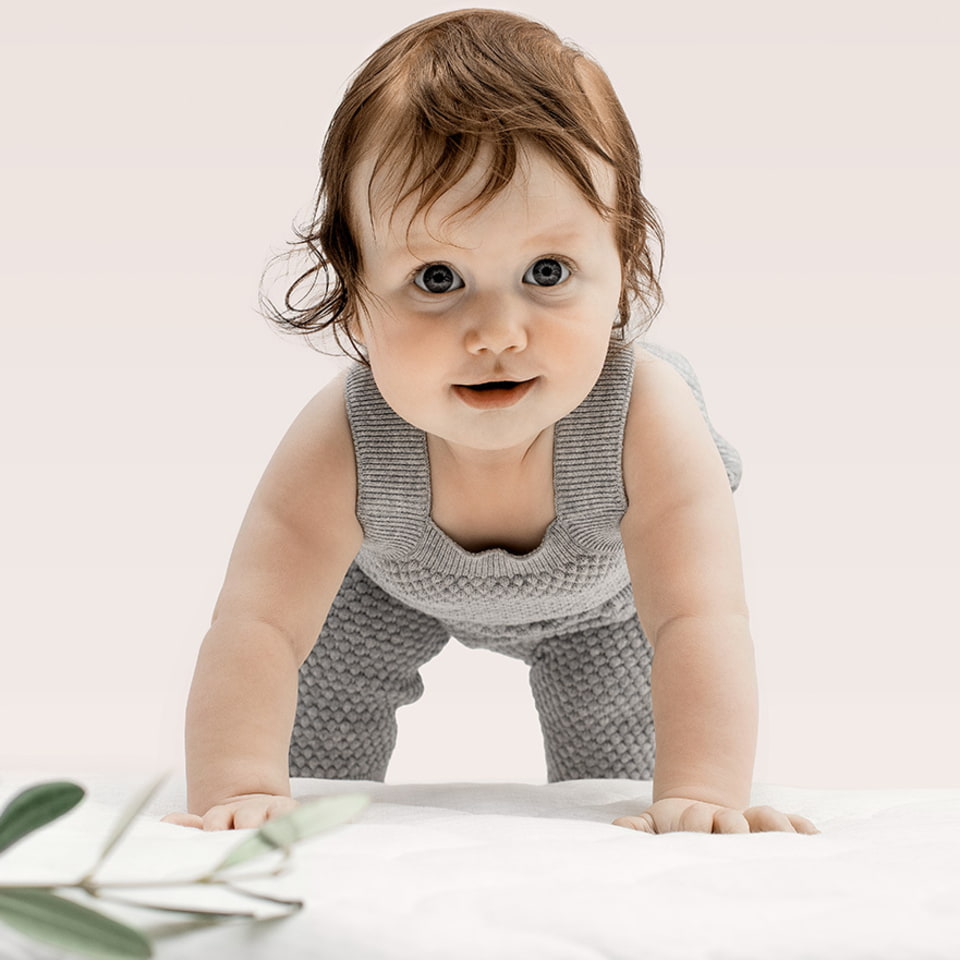 Bébé en grenouillère grise sur fond beige