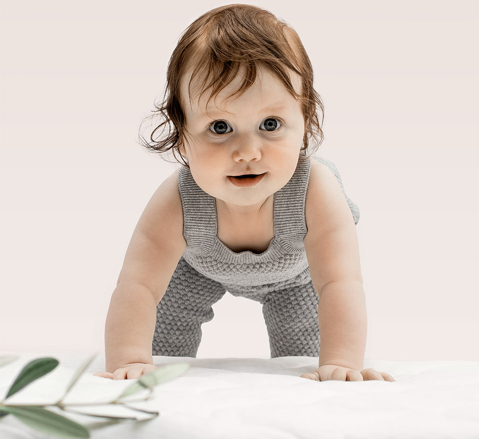 Bébé en grenouillère grise sur fond beige