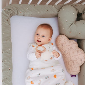 Baby im Babybett mit Bettschlange und Kuschelkissen