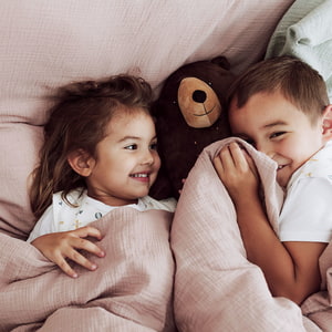 Geschwister kuscheln unter Baumwollmusselin Bettwäsche