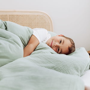 Kind im großen Bett mit Bettwäsche aus Baumwollmusselin