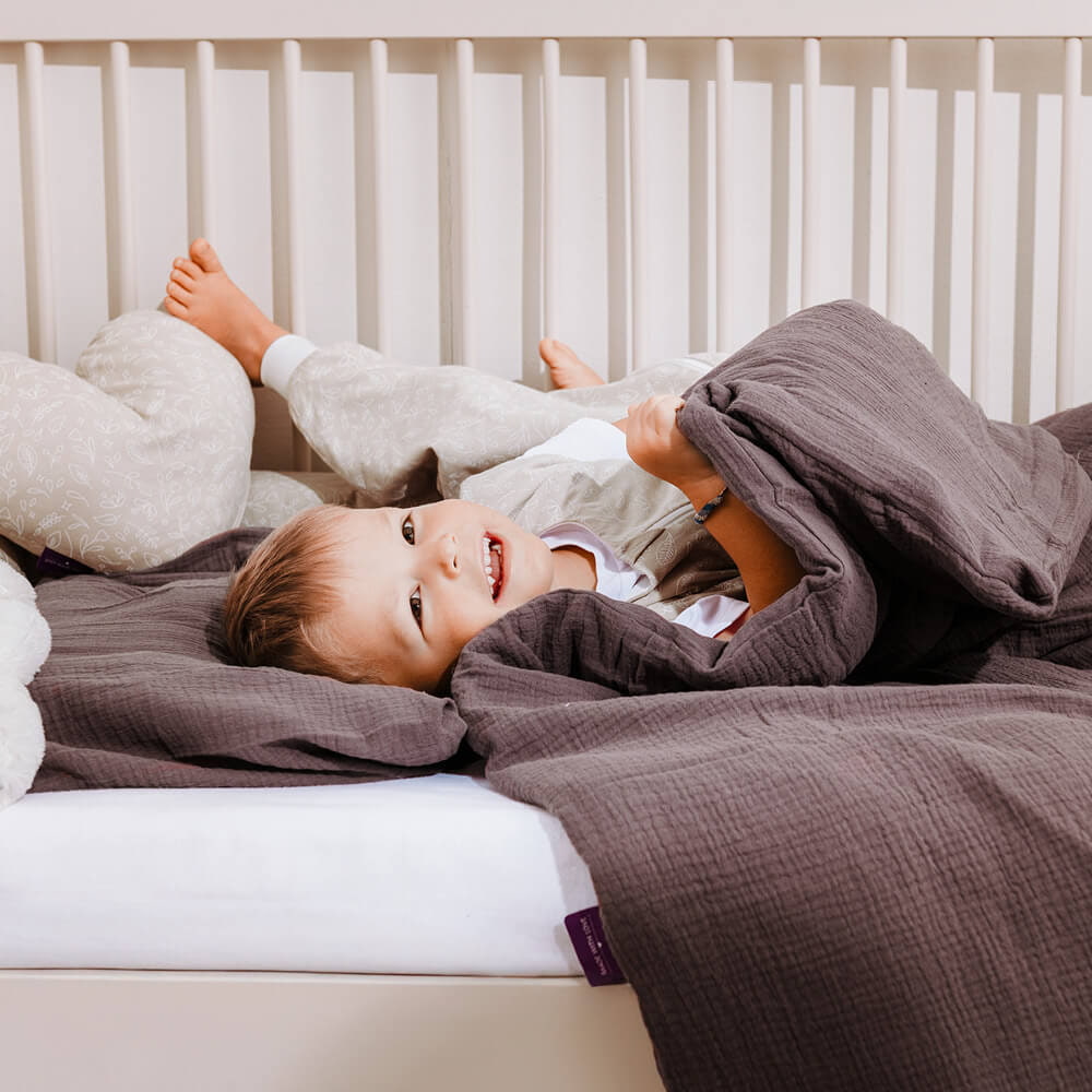 Kind kuschelt im Bett mit kuscheliger Bettwäsche